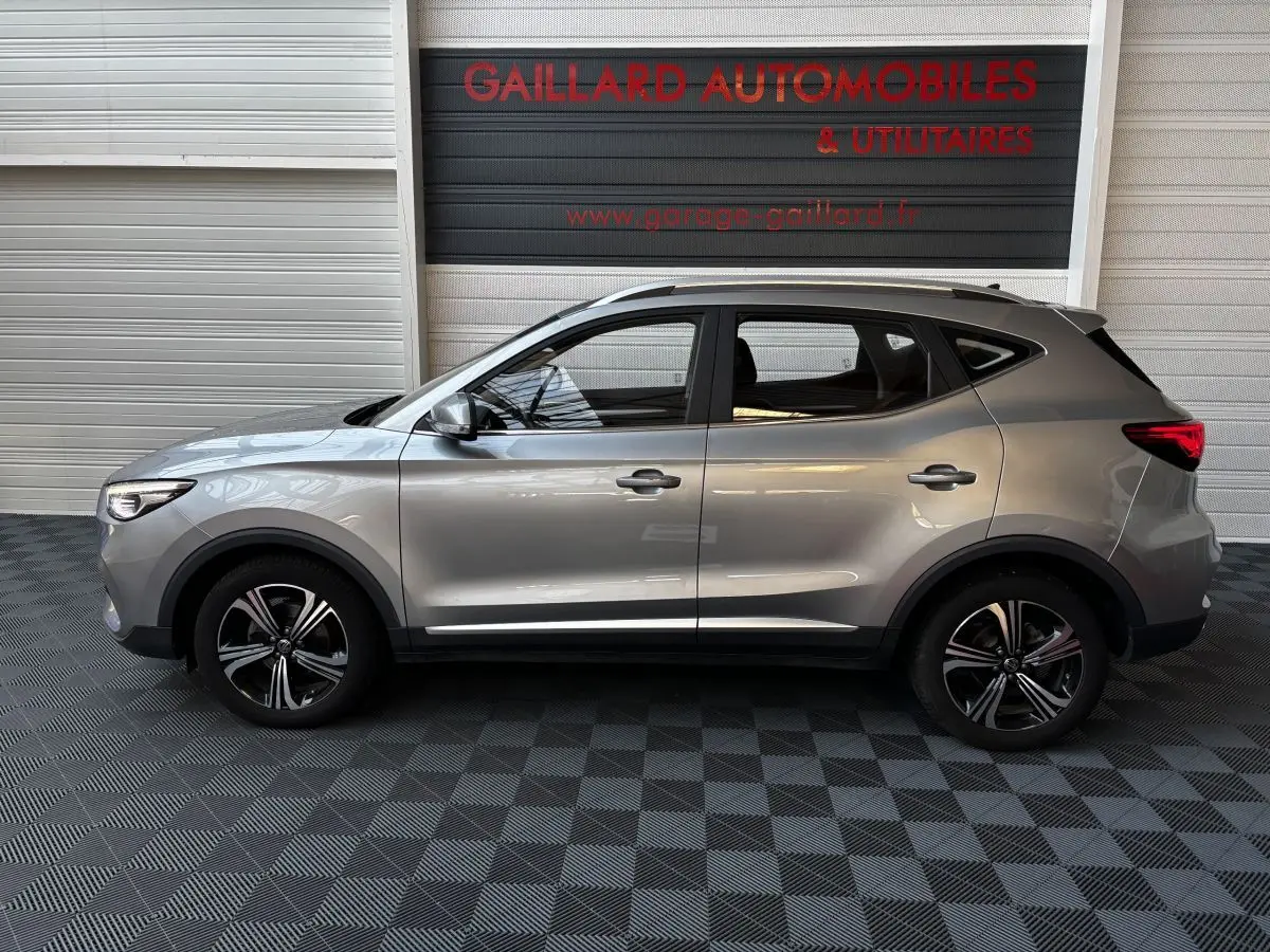 Vue de profil côté gauche d'un MG ZS gris clair 2022 avec jantes alliage et barres de toit chromées.