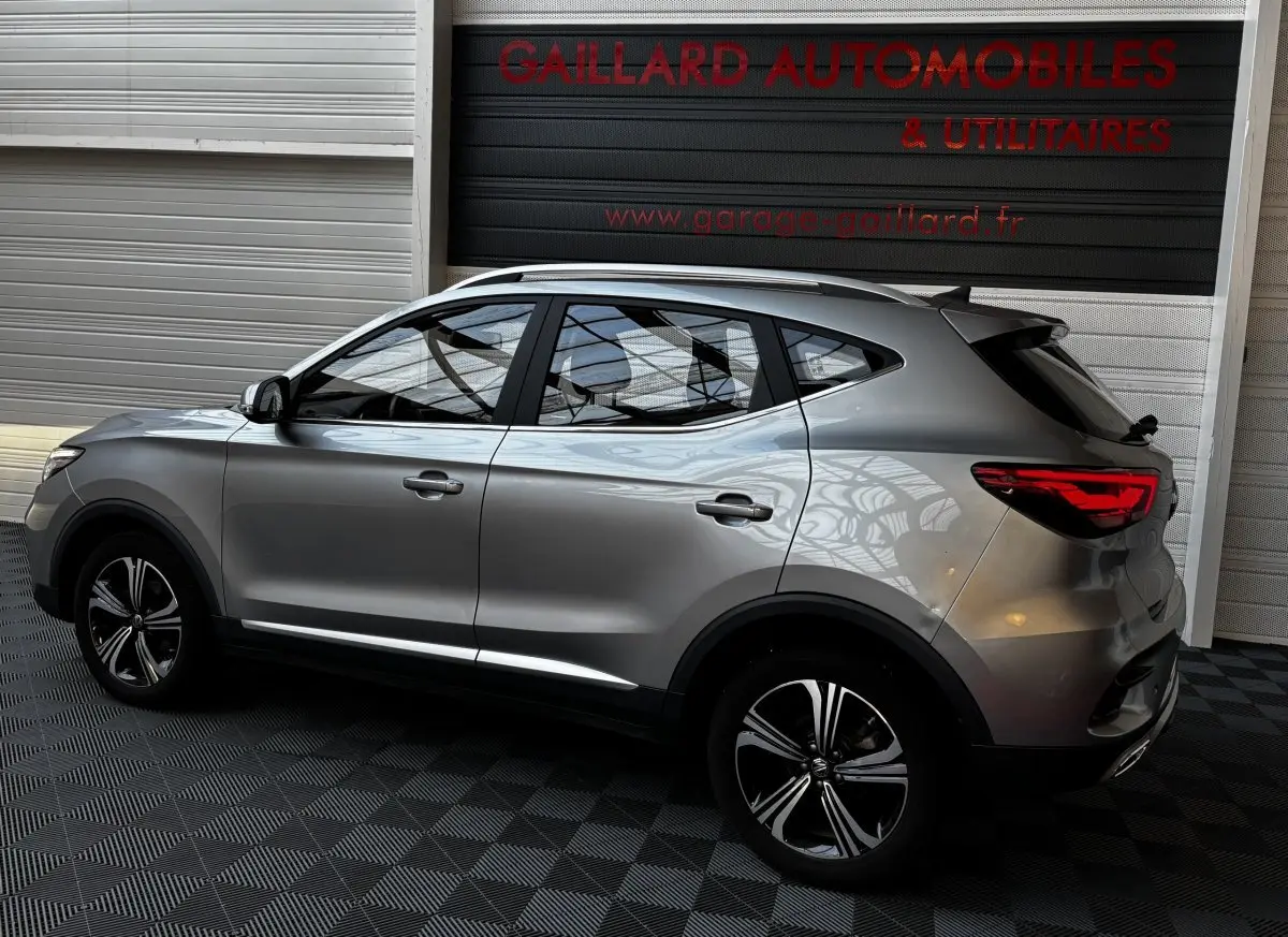 Vue de profil côté gauche d'un MG ZS gris clair 2022 avec jantes alliage et barres de toit chromées.