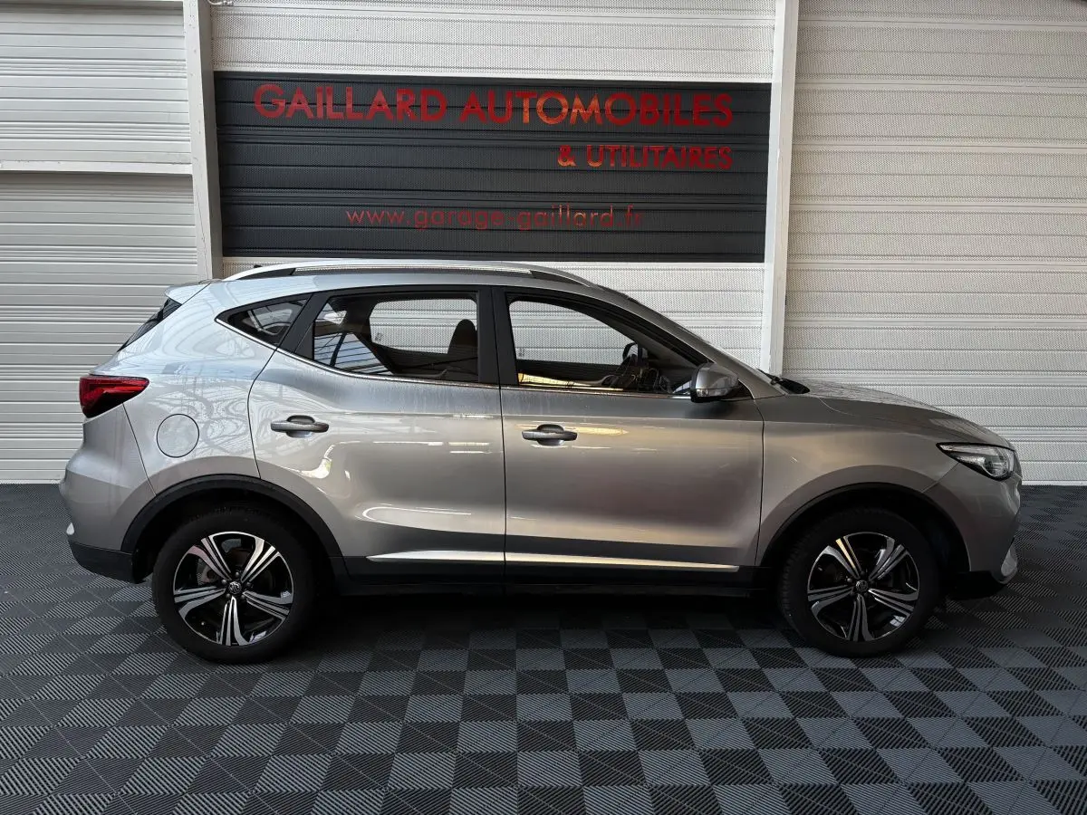 Vue latérale droite d'un SUV MG ZS gris clair 2022 avec jantes alliage et barres de toit chromées.