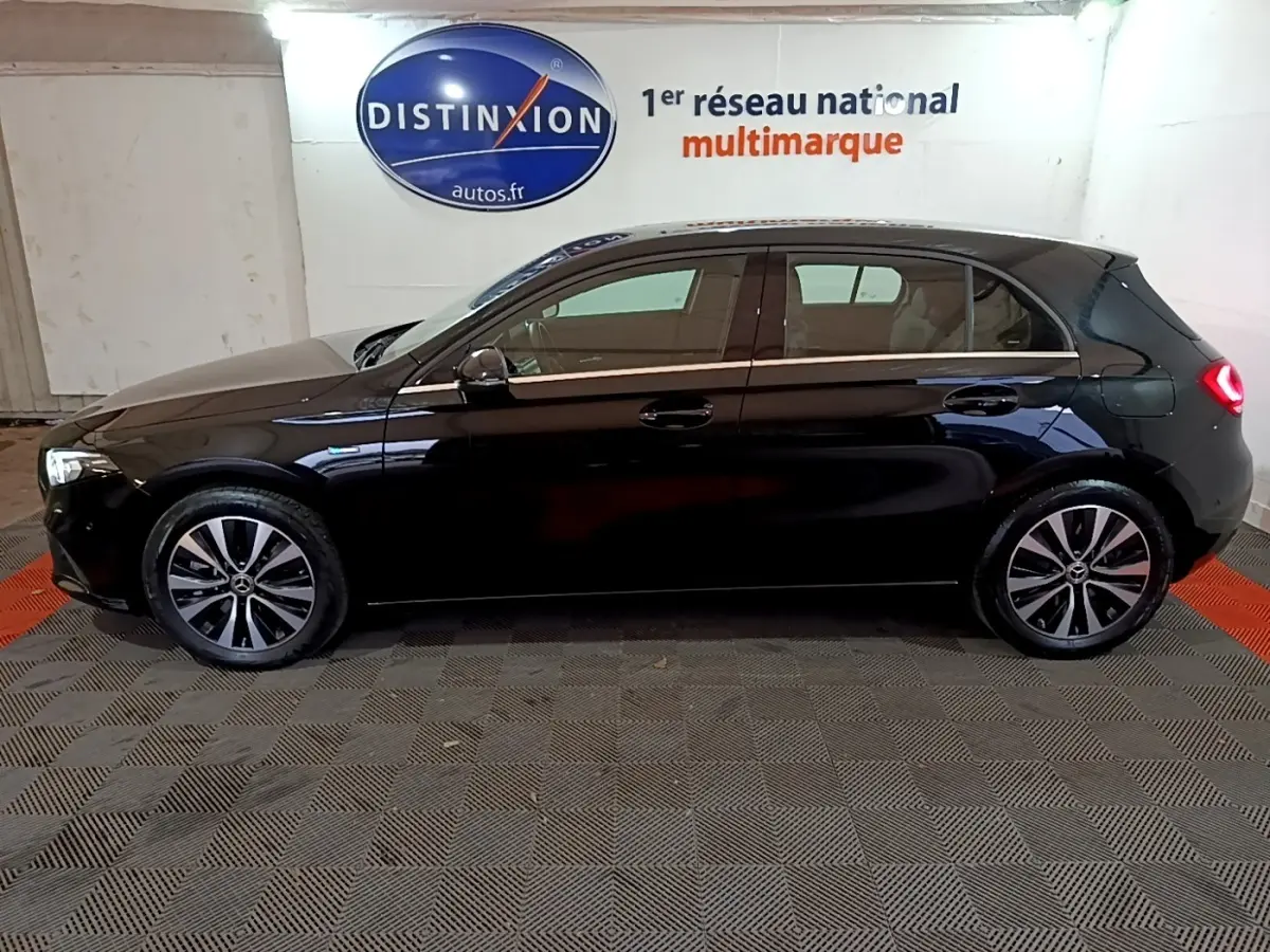 Vue de profil côté gauche d'une Mercedes Classe A 250 e Business Line noire avec feux arrière allumés en intérieur showroom.