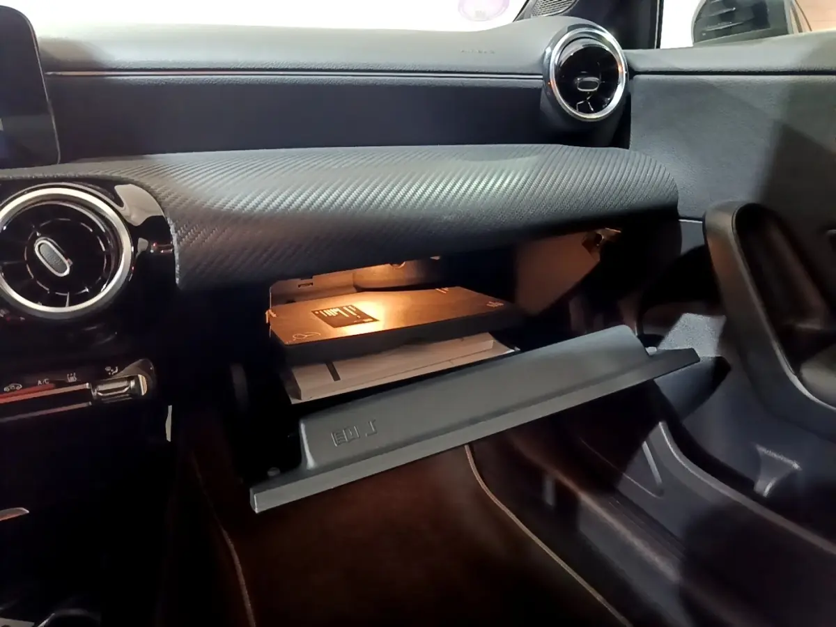Vue intérieure de la boîte à gants ouverte côté passager dans une Mercedes Classe A noire avec tableau de bord texturé.