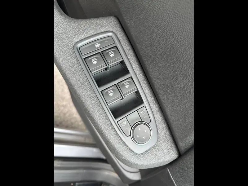 Gros plan sur les commandes des vitres électriques et réglages des rétroviseurs côté conducteur de la Renault Clio gris Rafale 2025.