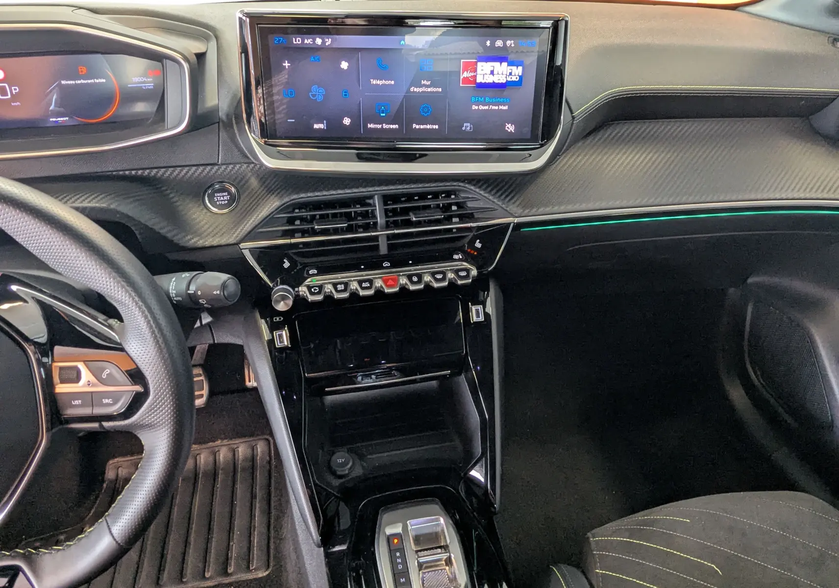 Vue intérieure du tableau de bord et console centrale de la Peugeot 208 Hybrid 145 GT 2025 avec écran tactile et surpiqûres vertes.