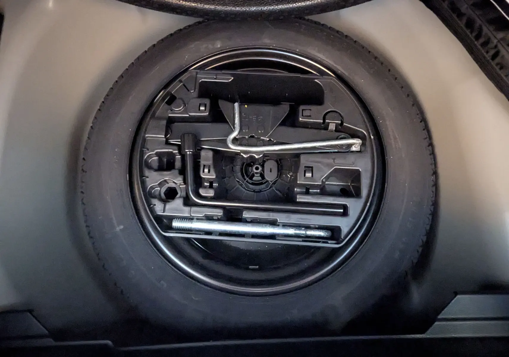 Gros plan sur la roue de secours et son kit d'outils intégrés dans le coffre d'une Peugeot 208 Hybrid 145 gris selenium.