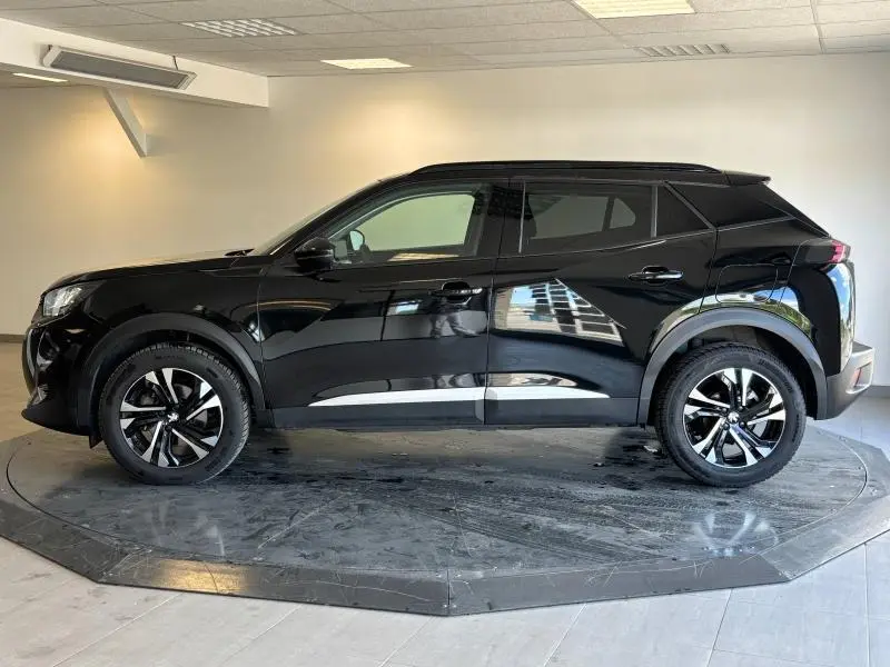 Peugeot 2008 noir Perla Nera vue de profil côté gauche, avec jantes alu et barres de toit visibles.