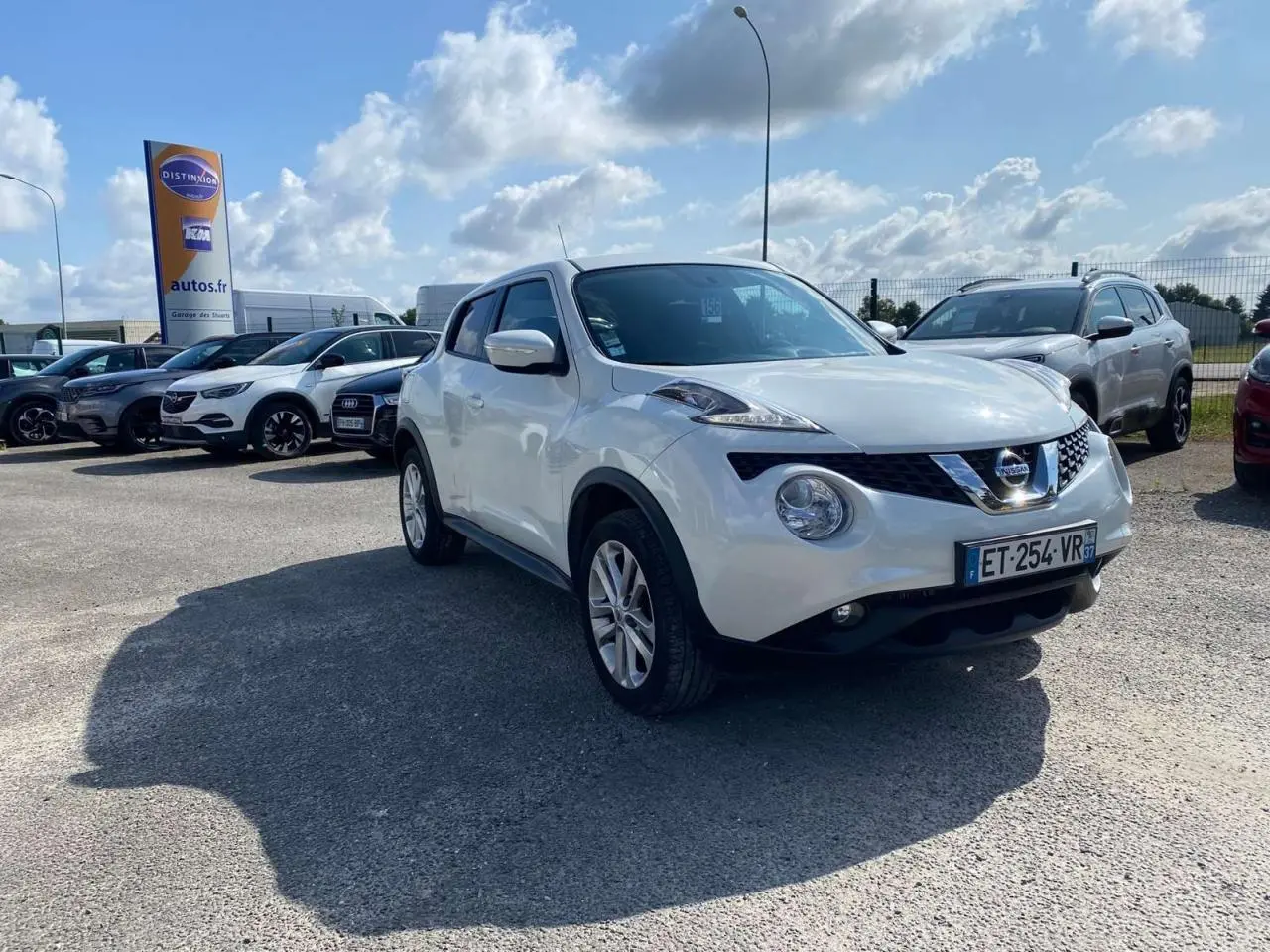 Nissan Juke blanc en 3/4 avant droit sur parking, avec jantes alliage 17 pouces sport visibles.