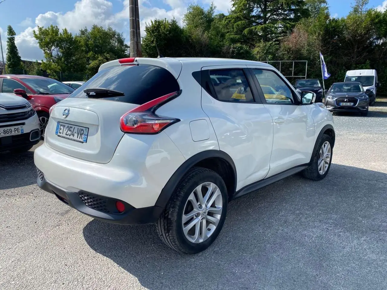 Nissan Juke blanc métallisé vu en 3/4 arrière droit, avec jantes alliage 17 pouces sport et vitres arrière surteintées.