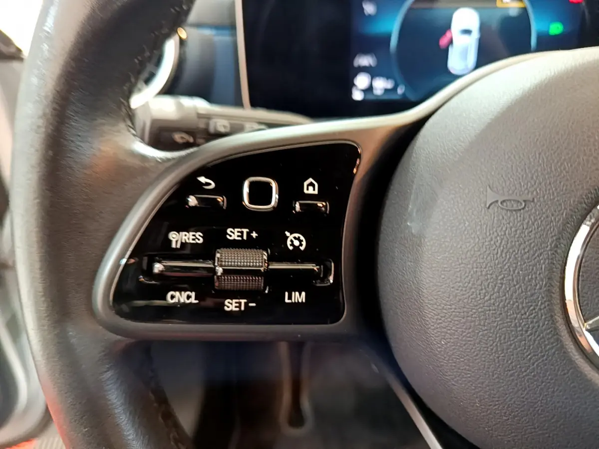 Gros plan sur les commandes de régulateur de vitesse au volant cuir d’une Mercedes Classe A gris clair de 2020.