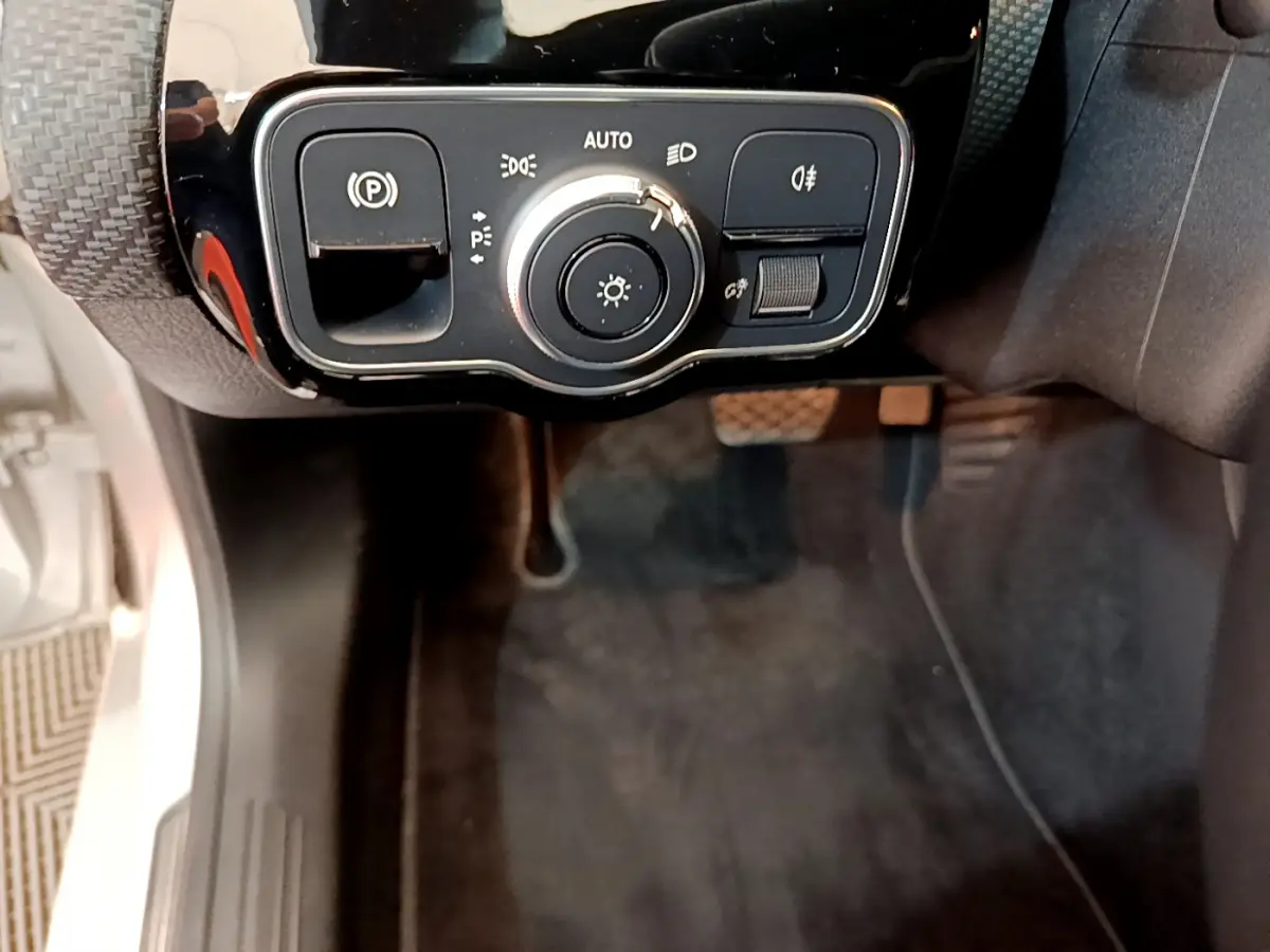 Gros plan sur la commande des phares et frein à main électrique côté gauche d’une Mercedes Classe A gris clair.