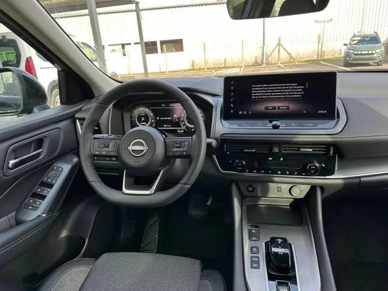 Vue intérieure avant du Nissan Qashqai Hybrid e-POWER 2025, tableau de bord noir avec écran tactile large et volant multifonction.