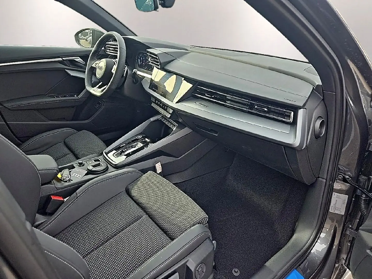Intérieur avant droit de l'Audi A3 Sportback gris Daytona, avec tableau de bord moderne et sièges sport noirs.