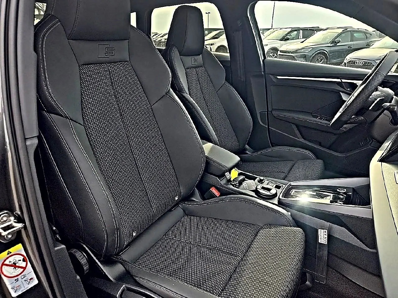 Vue intérieure côté conducteur de l’Audi A3 Sportback 2026 avec sièges sport noirs et surpiqûres contrastées.