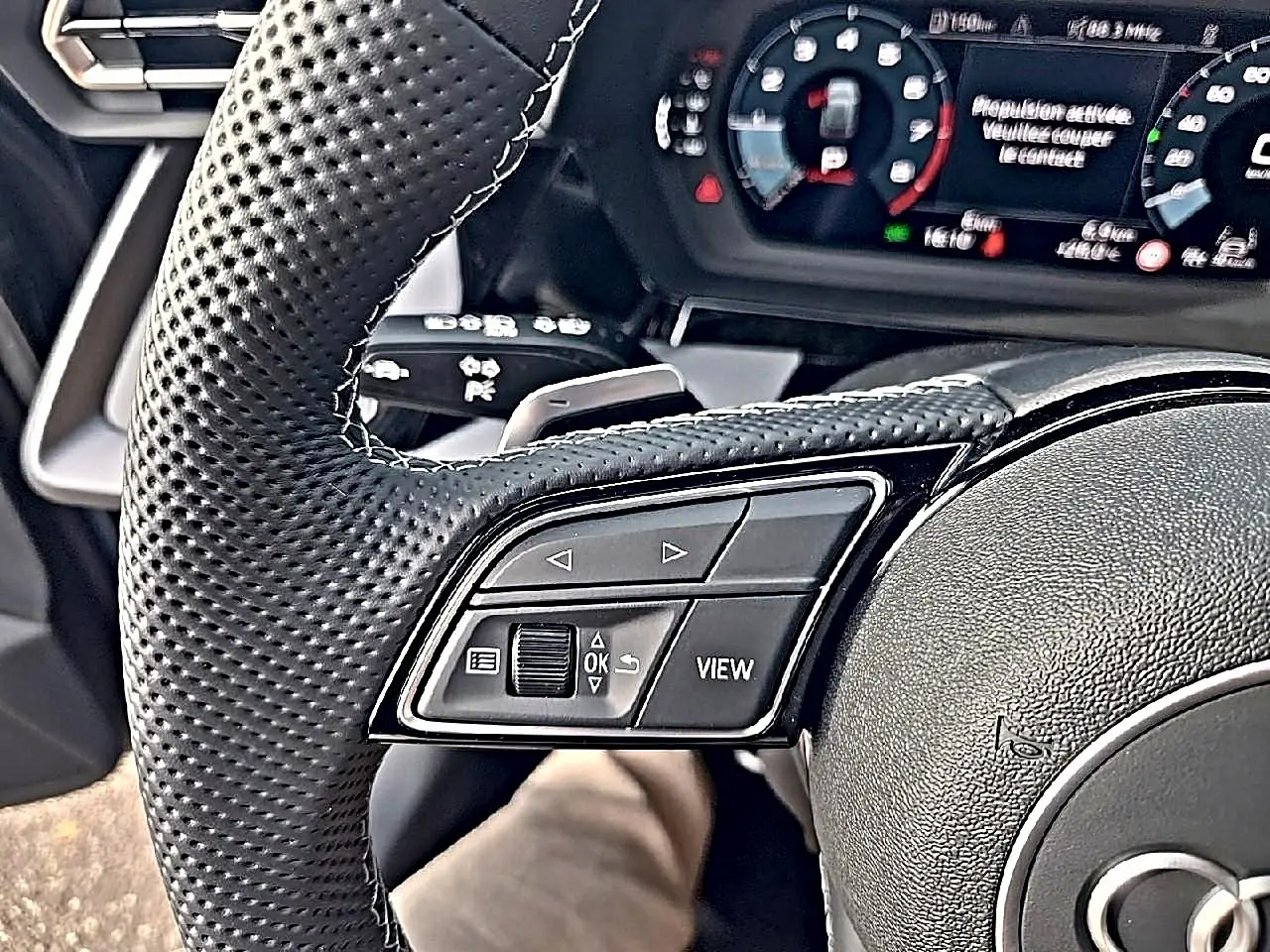 Gros plan sur le volant cuir perforé et les commandes multifonctions à gauche de l'Audi A3 Sportback gris Daytona 2026.