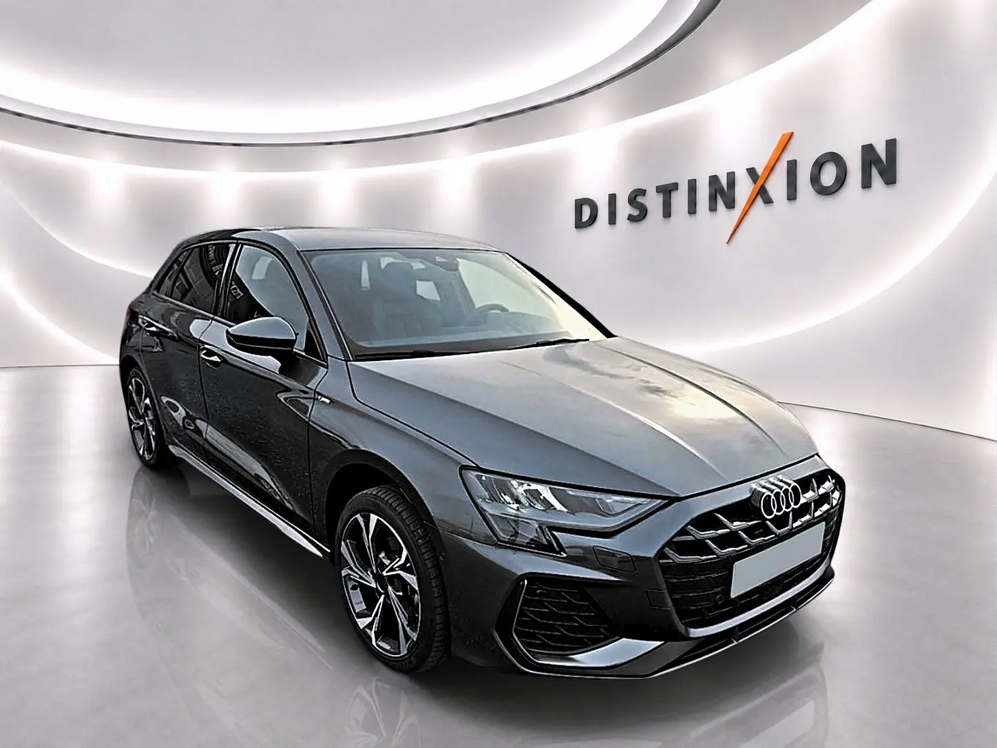 Audi A3 Sportback gris Daytona vue 3/4 avant droit dans un showroom lumineux avec logo Distinxion en arrière-plan.