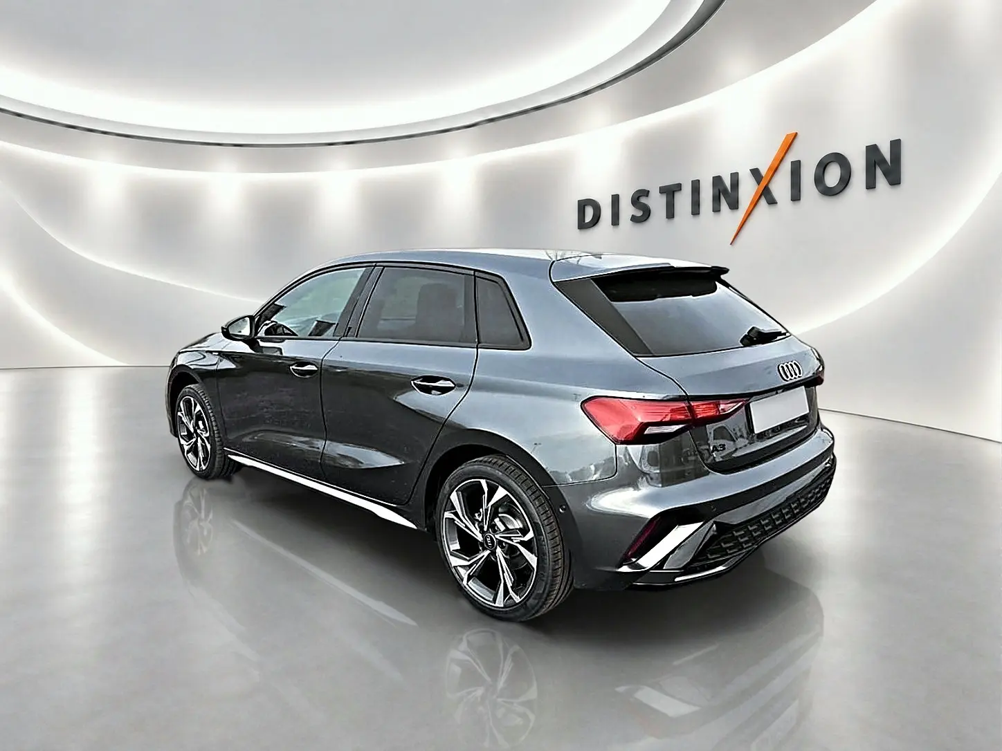 Audi A3 Sportback gris Daytona vue 3/4 arrière droit dans un showroom lumineux avec jantes alu distinctives.