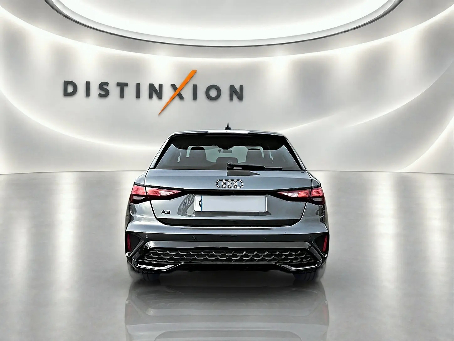 Vue arrière d'une Audi A3 Sportback gris Daytona 2026 dans un showroom lumineux avec logo Distinxion en arrière-plan.