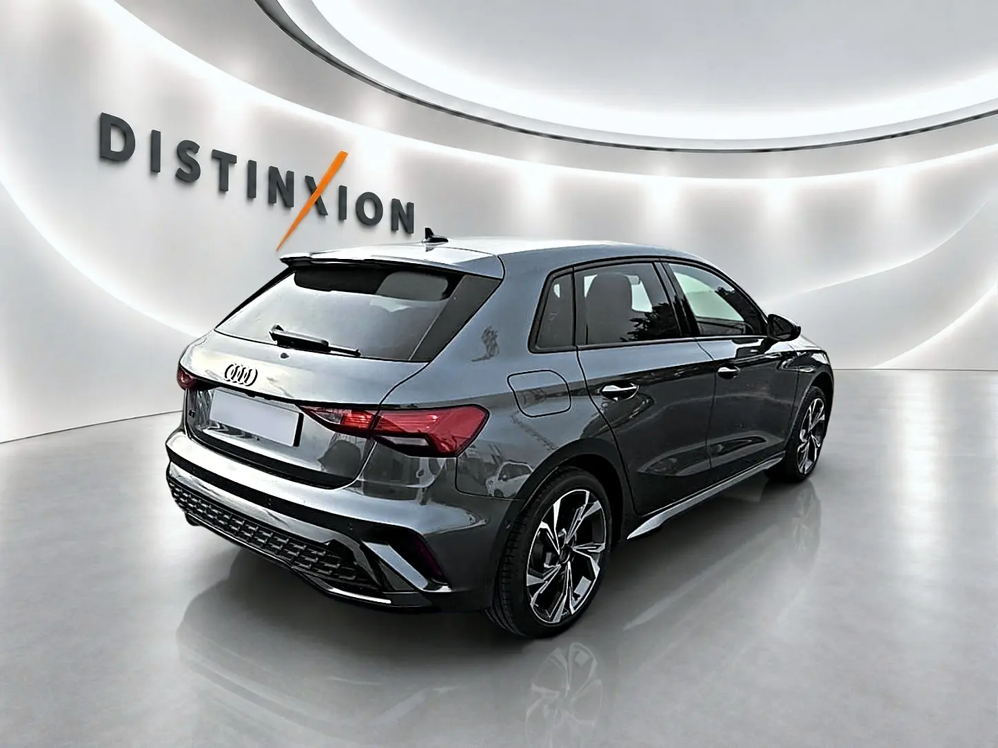 Audi A3 Sportback gris Daytona vue 3/4 arrière droit dans un showroom lumineux avec jantes alu distinctives.