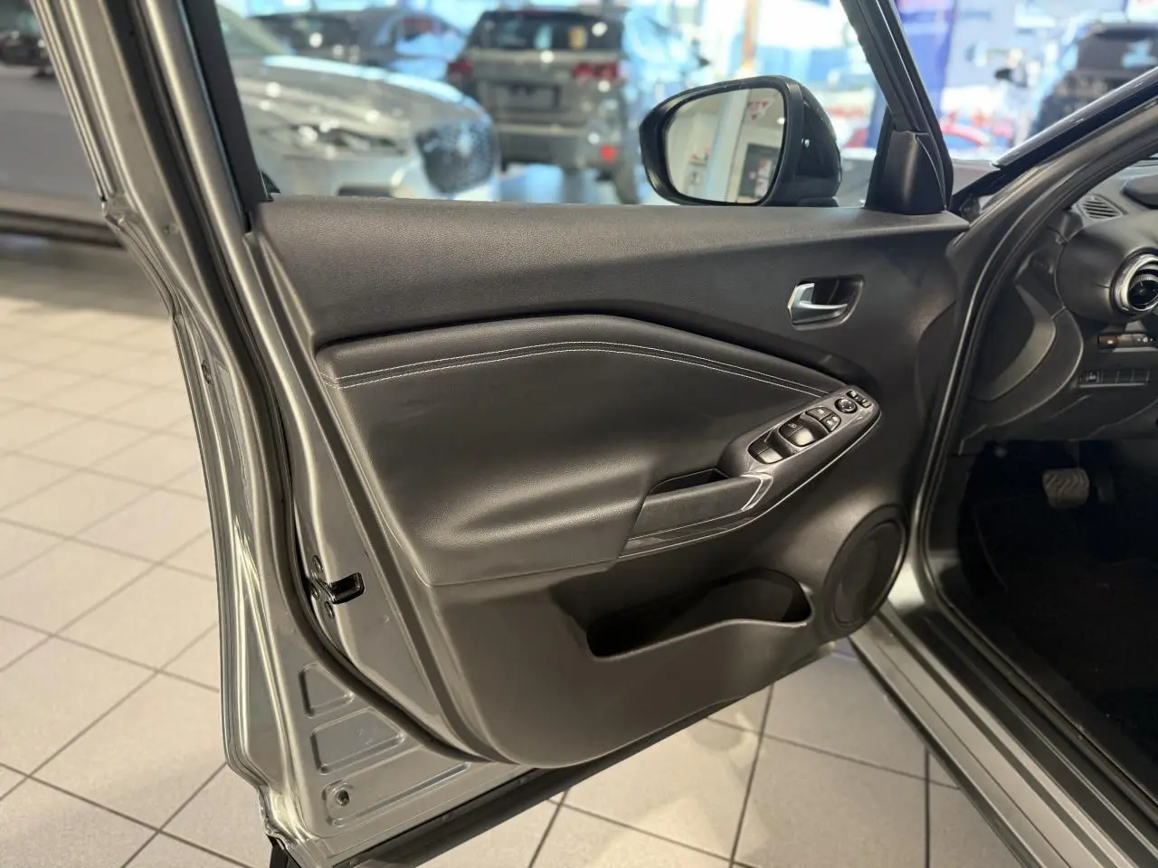 Vue rapprochée de la porte avant gauche gris métallisé du Nissan Juke Hybrid 143 N-Connecta avec commandes de vitres et haut-parleur intégré.