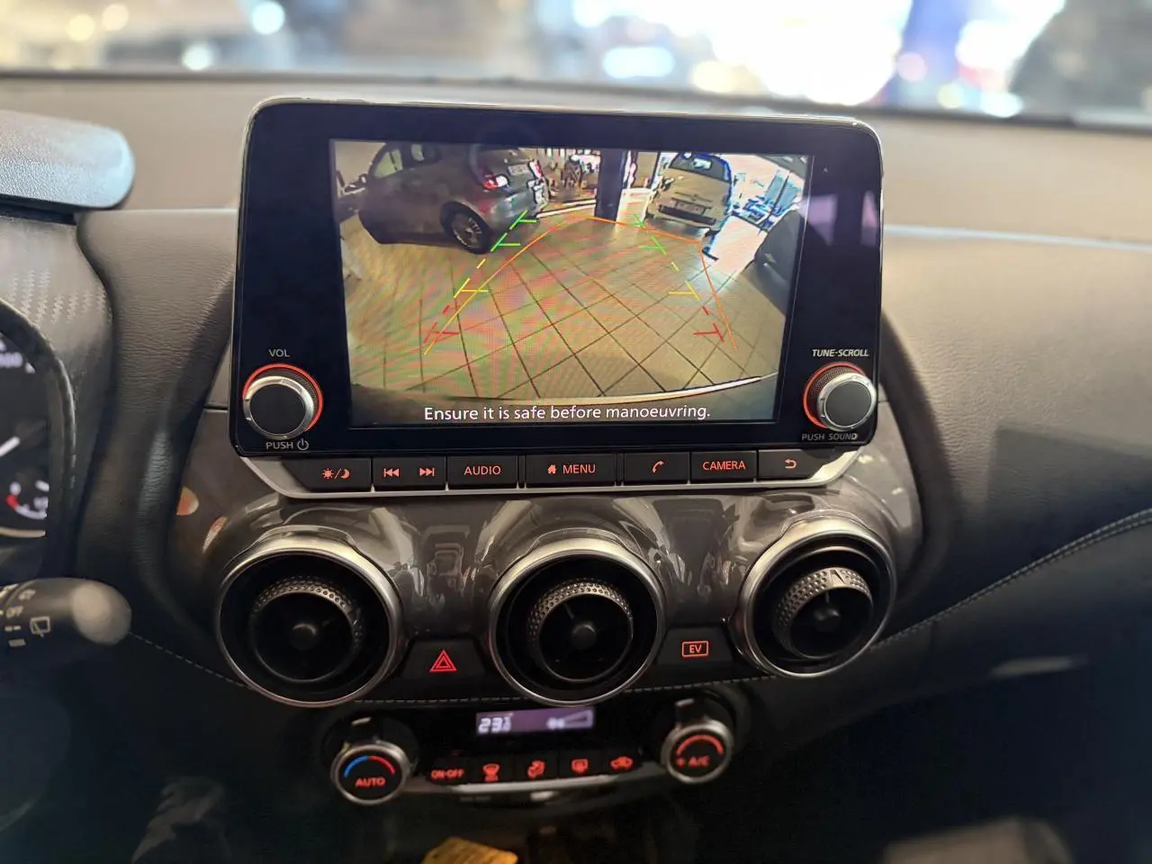 Vue rapprochée du tableau de bord du Nissan Juke Hybrid 2024 avec écran de caméra de recul et commandes de climatisation.