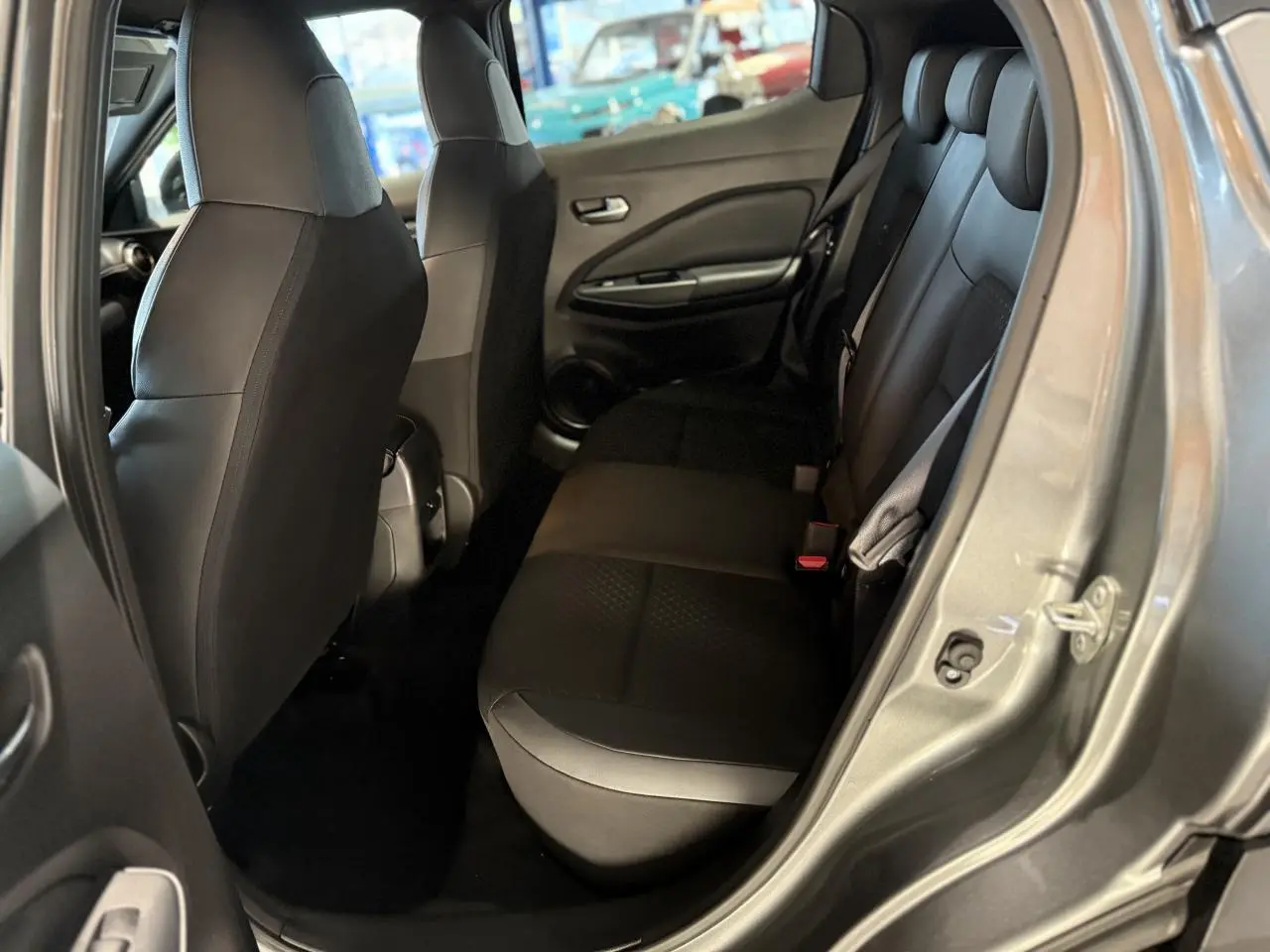 Vue intérieure côté arrière droit du Nissan Juke Hybrid 143 N-Connecta gris métallisé, montrant la banquette arrière en tissu noir.