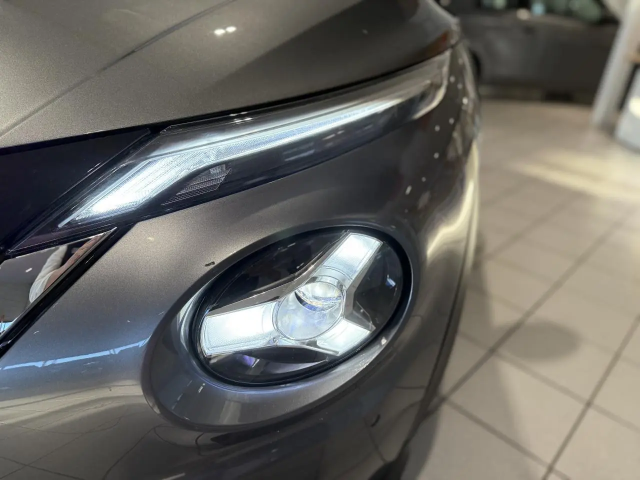 Gros plan sur le phare avant droit allumé du Nissan Juke Hybrid gris métallisé, mettant en valeur son design LED distinctif.