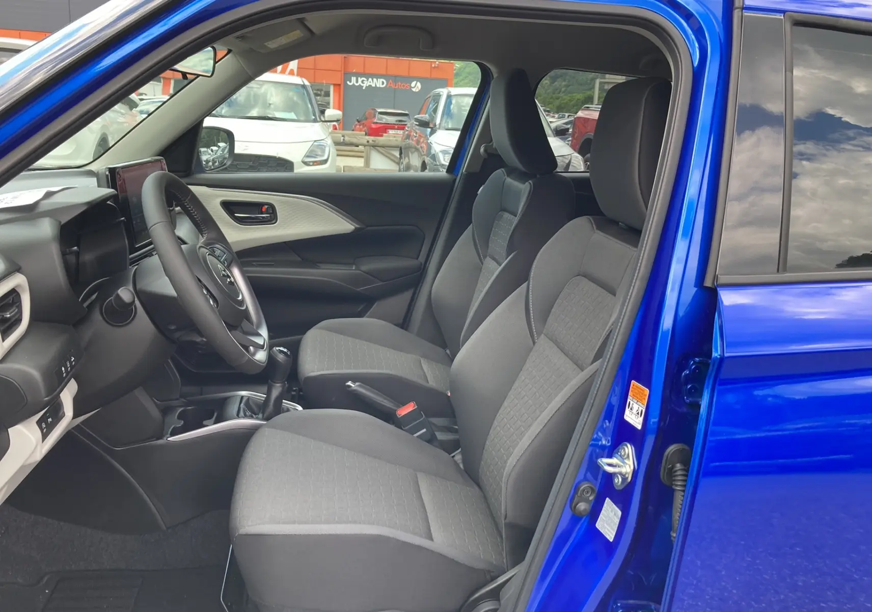 Intérieur de la Suzuki Swift 2025 en bleu Frontier, vue côté gauche montrant sièges tissu et volant cuir multifonctions.