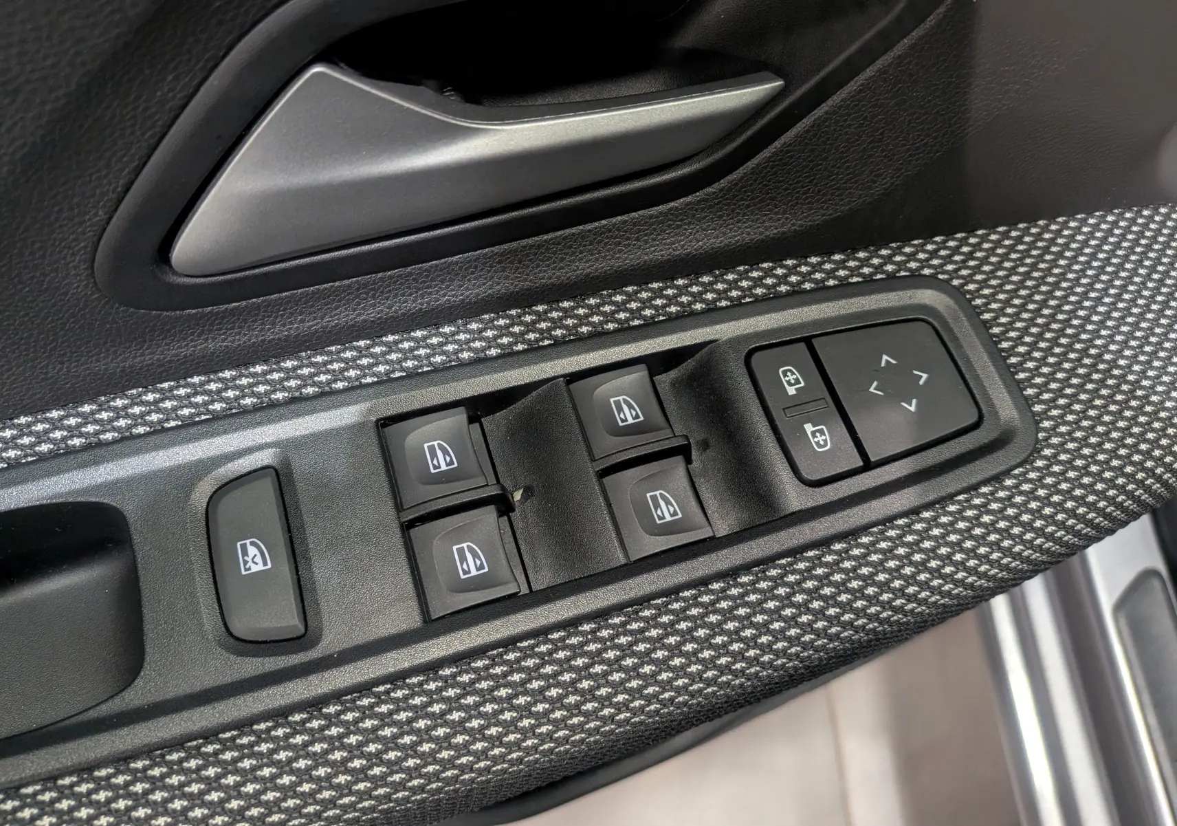 Gros plan sur la commande des vitres électriques côté gauche avec tissu gris et poignée argentée dans une Dacia Sandero 2025.