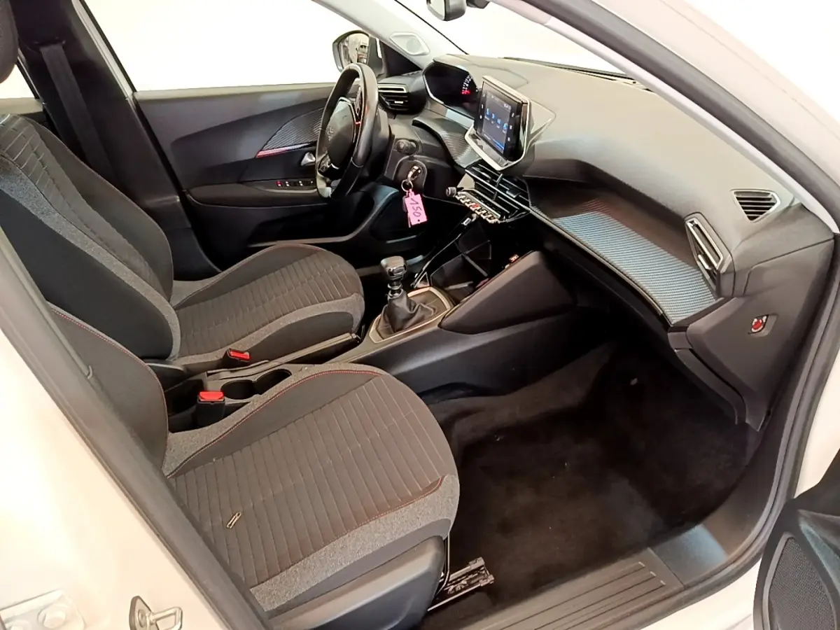 Vue intérieure côté conducteur du Peugeot 2008 blanc, montrant le tableau de bord et la console centrale avec écran tactile.