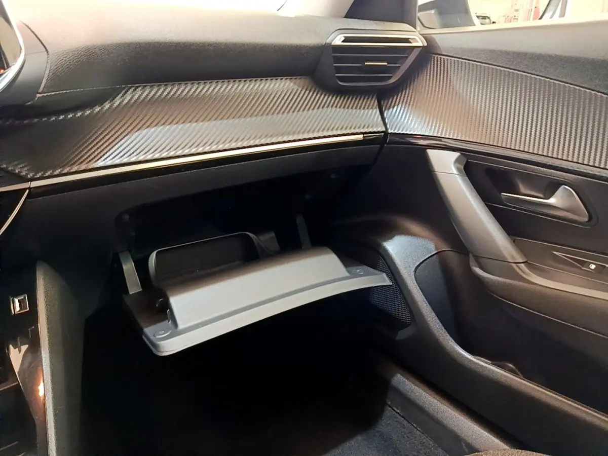 Intérieur noir de la Peugeot 2008, vue côté passager avec boîte à gants ouverte et tableau de bord effet carbone.