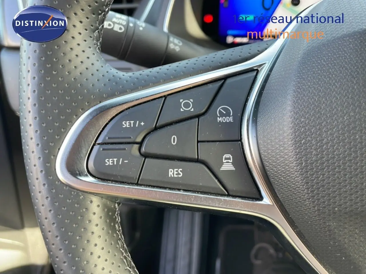 Gros plan sur les commandes au volant en cuir perforé noir de la Renault Symbioz 2025, avec écran digital flou en arrière-plan.