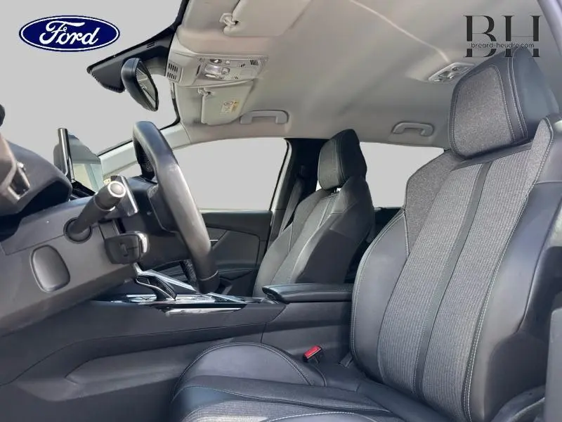 Vue intérieure côté conducteur d'un Peugeot 5008 blanc nacré, sièges en tissu et cuir noir avec console centrale visible.