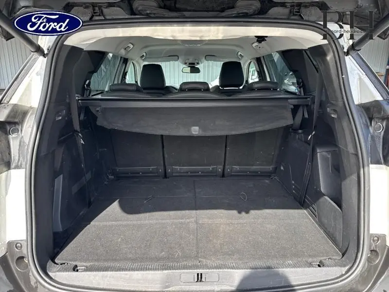 Coffre ouvert vu de l'arrière d'un Peugeot 5008 blanc nacré, avec cache-bagages et sièges arrière noirs.