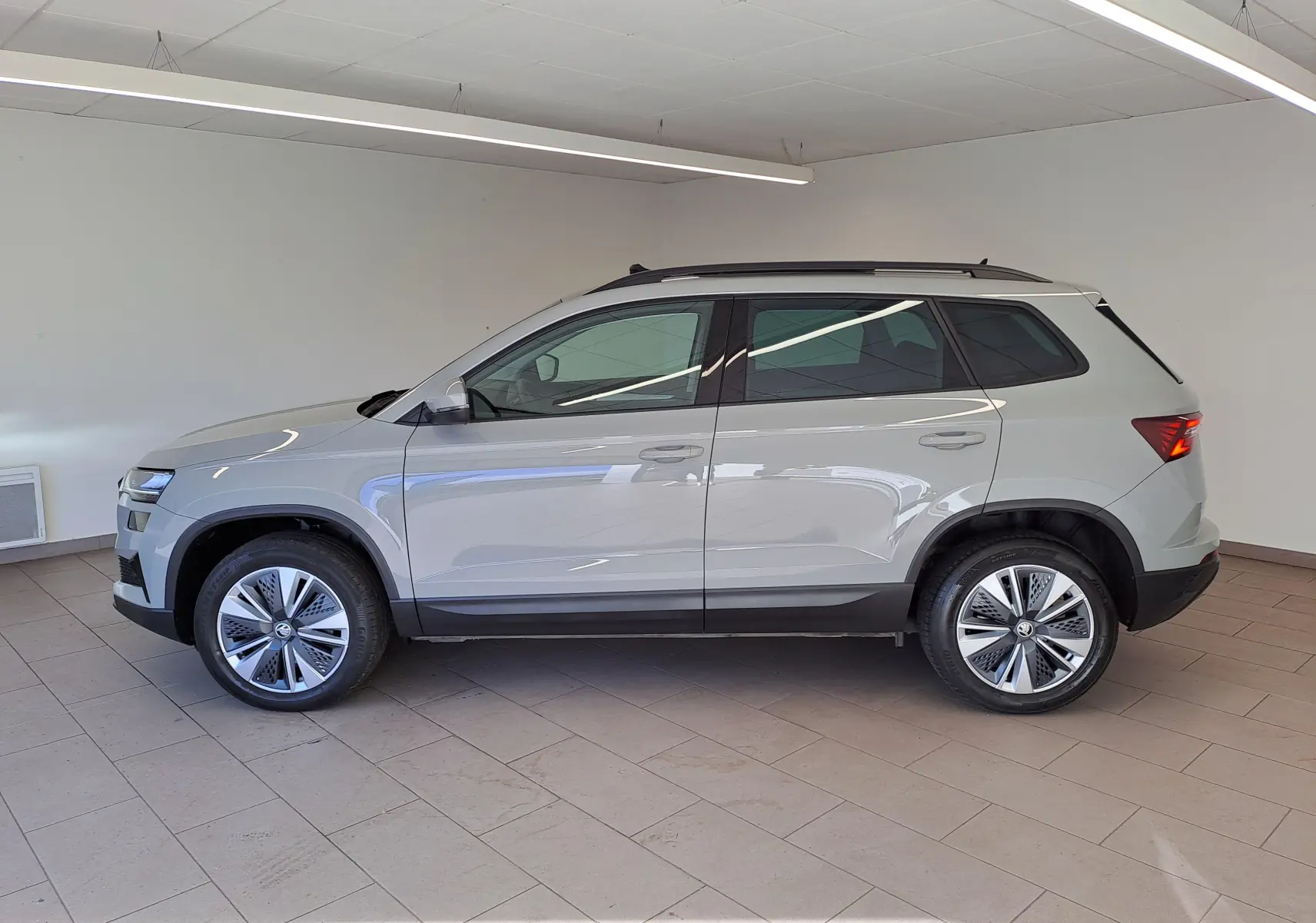 Vue de profil côté gauche du Skoda Karoq gris perle 2023 avec toit ouvrant panoramique et jantes alliage.