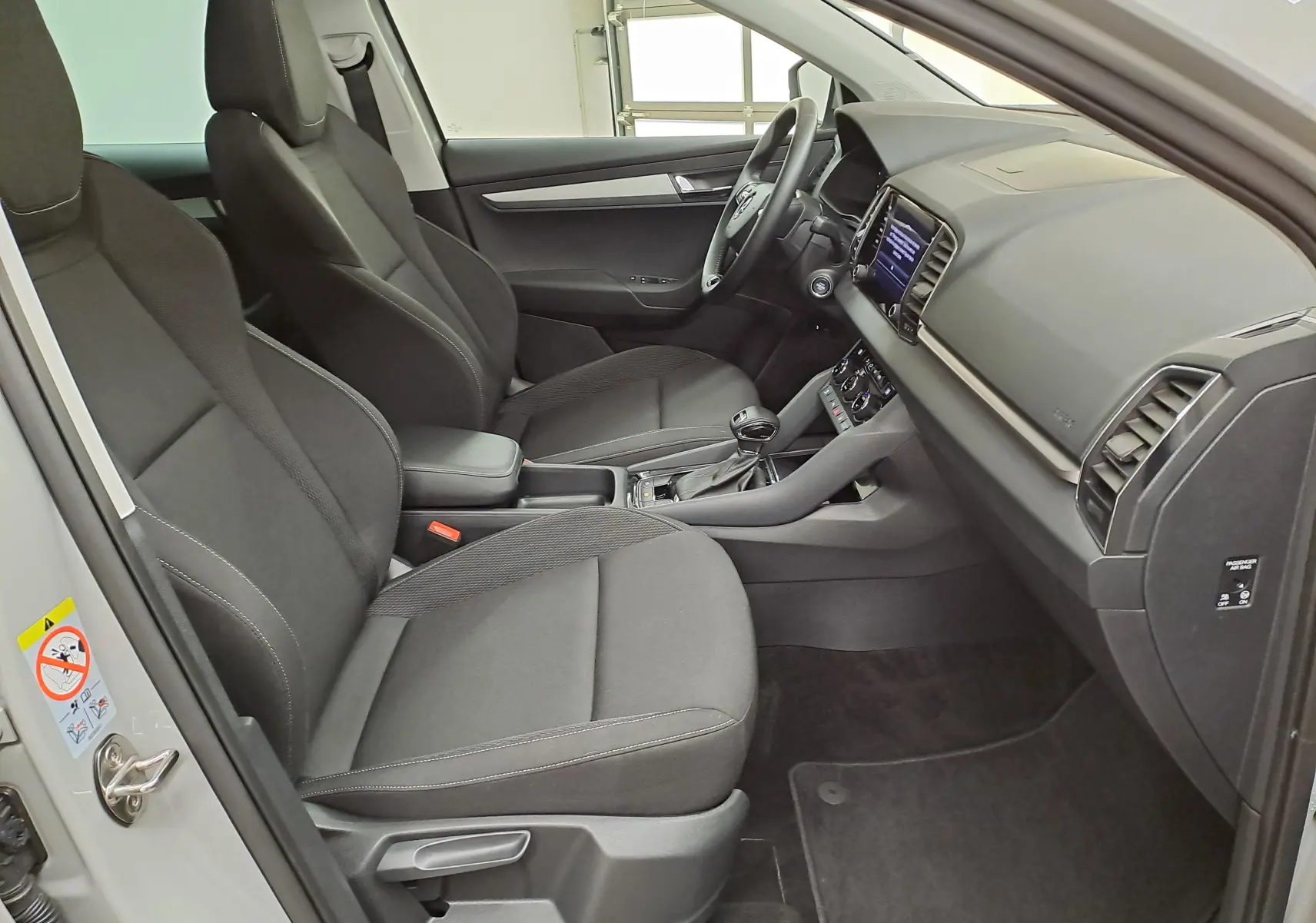 Vue intérieure côté conducteur du Skoda Karoq 2023 gris perle, mettant en valeur les sièges noirs et le tableau de bord moderne.