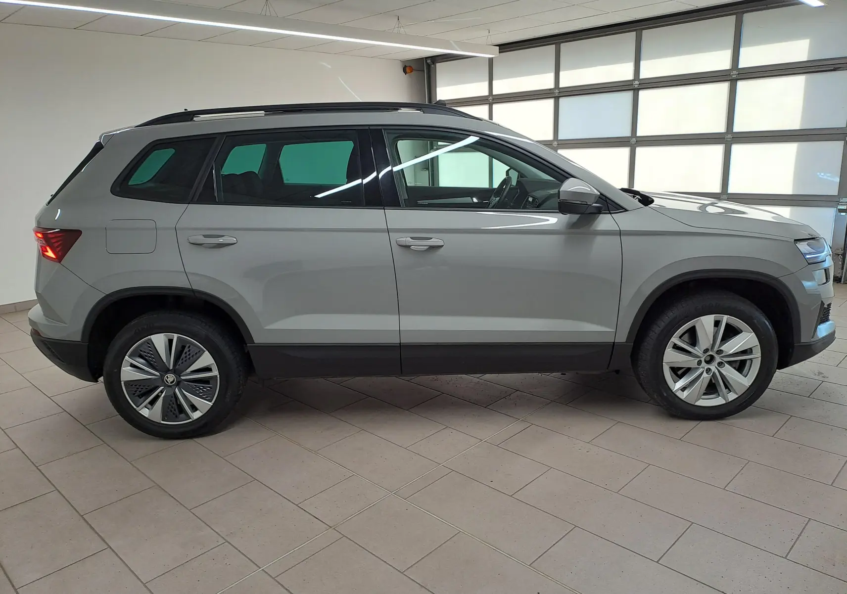 Vue de profil côté gauche d’un Skoda Karoq gris perle 2023 avec toit ouvrant panoramique en intérieur showroom.