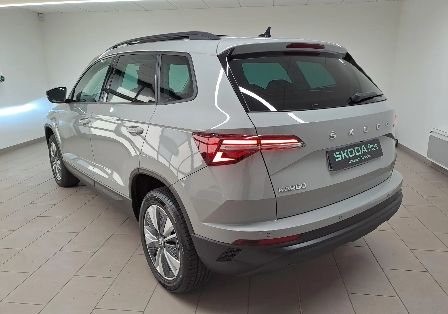 Vue 3/4 arrière droite d’un Skoda Karoq gris perle avec toit ouvrant panoramique dans un showroom.