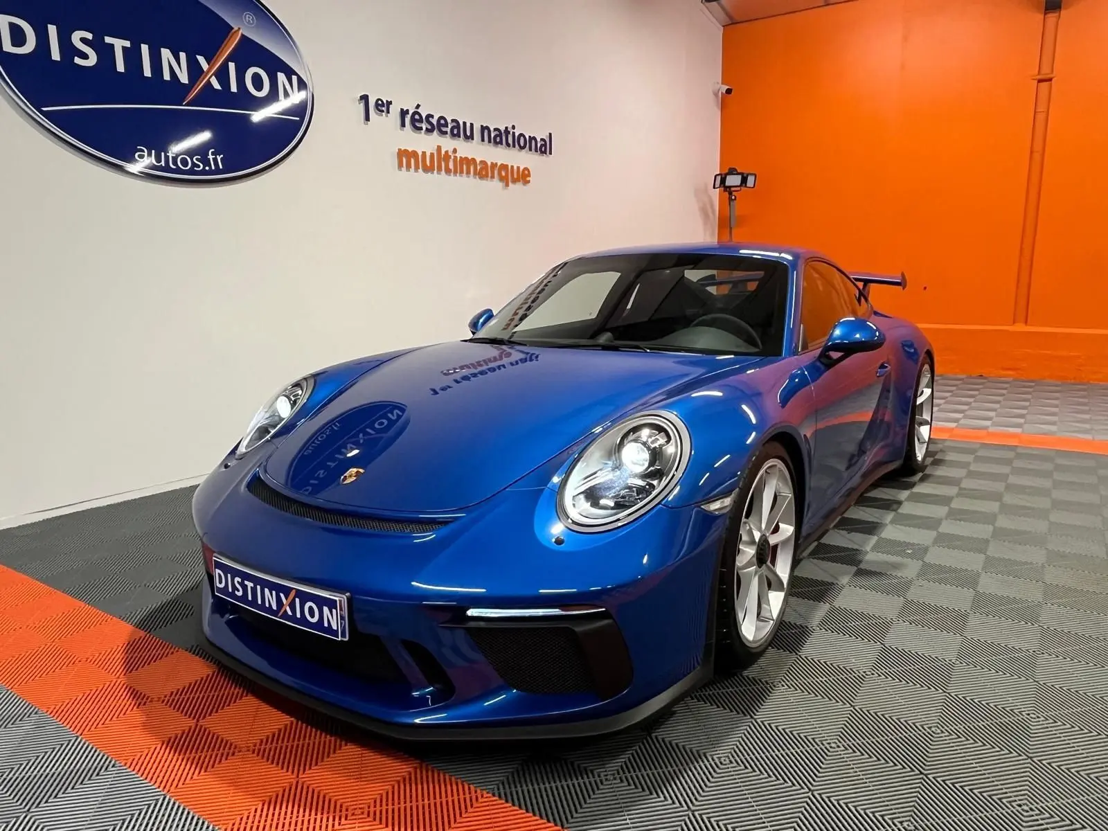 Porsche 911 GT3 bleu saphir vue 3/4 avant droit, avec aileron arrière et jantes argentées en showroom.