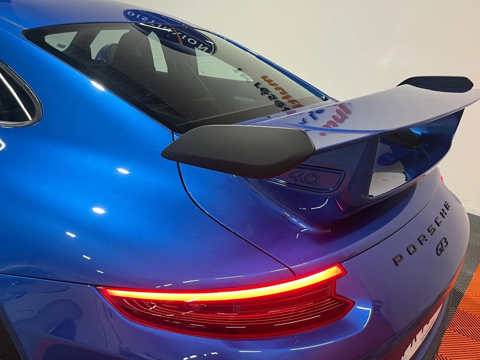 Vue 3/4 arrière droite d'une Porsche 911 GT3 bleu saphir avec aileron arrière et feux LED allumés.