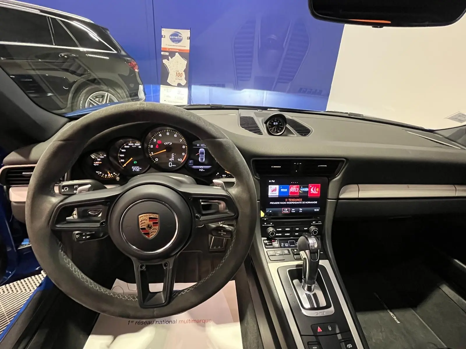 Vue intérieure centrée sur le volant sport alcantara et le tableau de bord de la Porsche 911 GT3 bleu saphir.