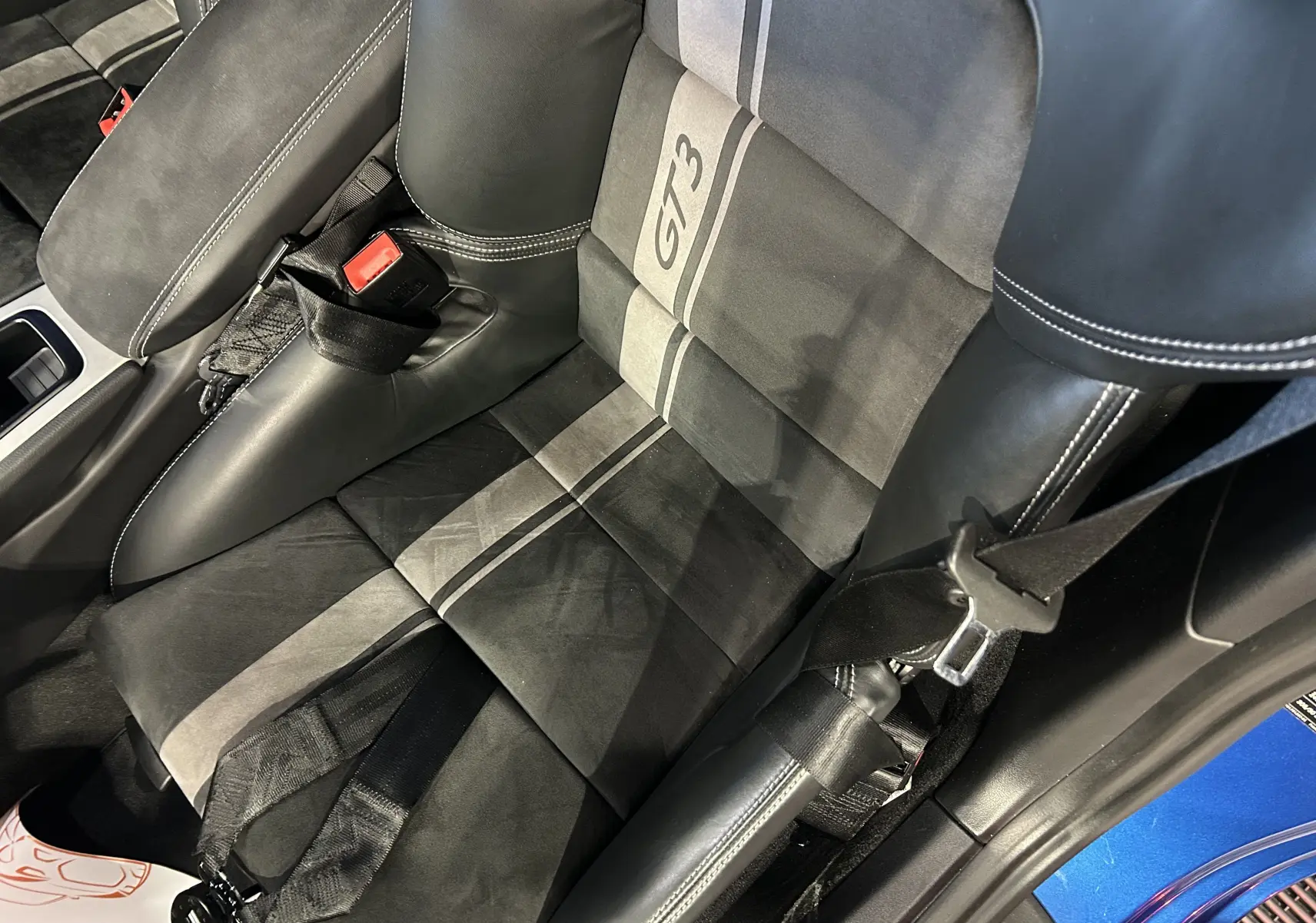 Gros plan sur le siège baquet sport alcantara noir et gris avec logo GT3, intérieur de Porsche 911 GT3 bleu saphir visible au bord.