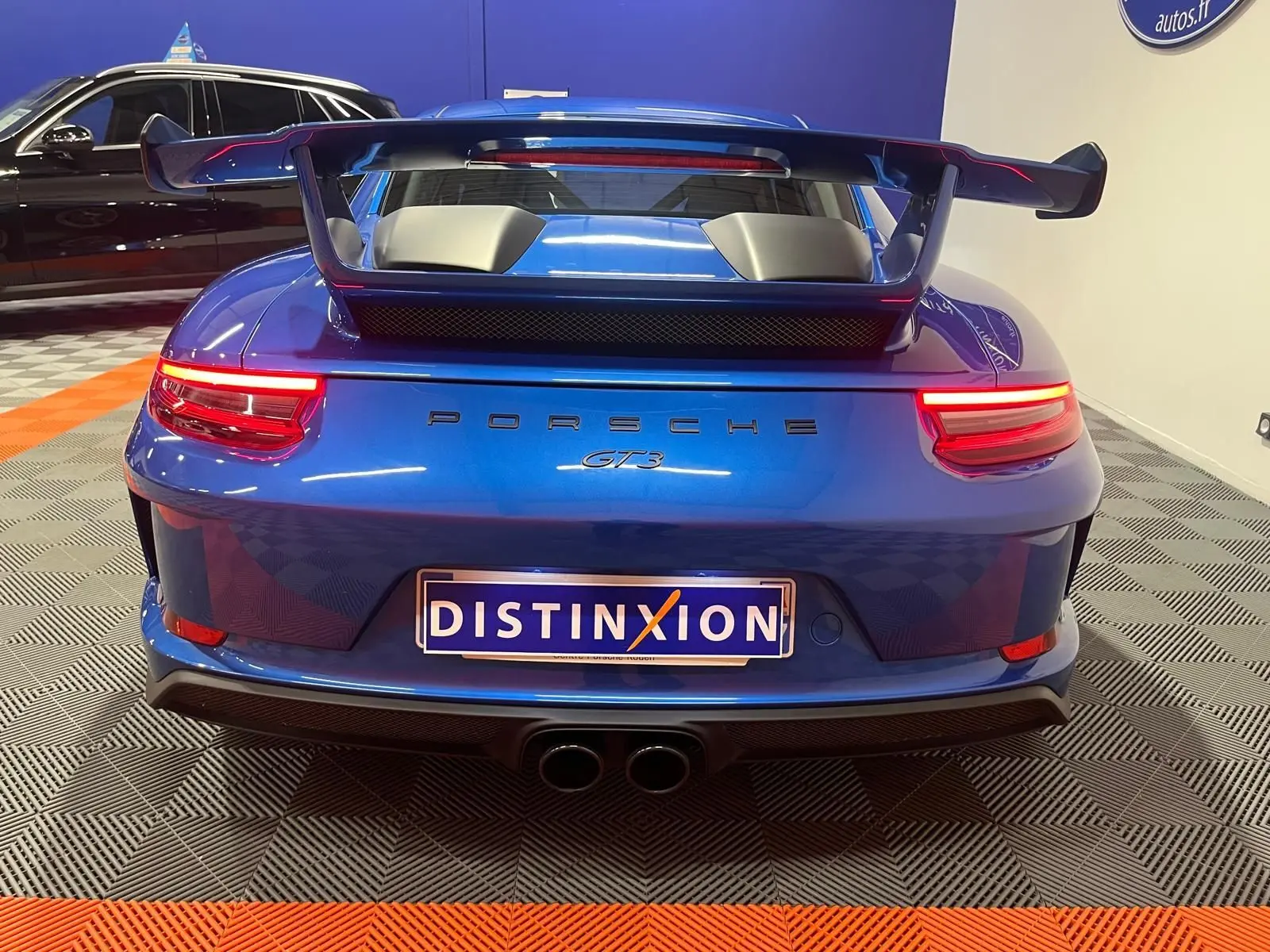 Vue arrière d'une Porsche 911 GT3 bleu saphir avec grand aileron et double sortie d'échappement centrale.