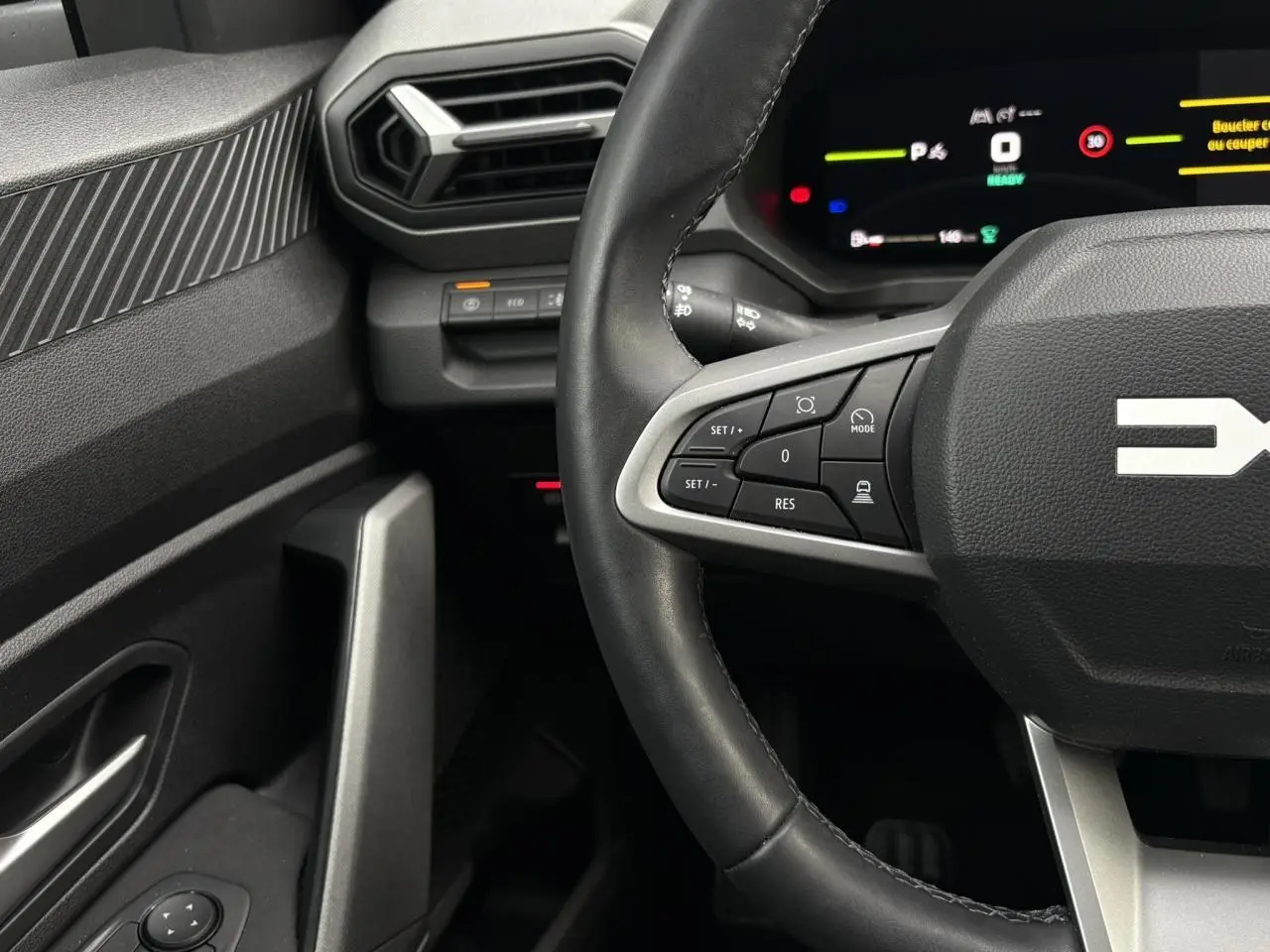 Vue intérieure centrée sur le volant noir du Dacia Bigster 2025, avec commandes multifonctions et tableau de bord numérique.