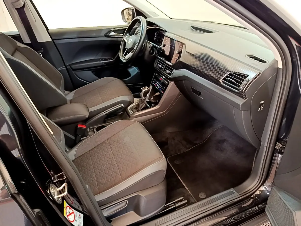 Vue intérieure côté conducteur du Volkswagen T-Cross noir, mettant en valeur le tableau de bord moderne et les sièges tissu gris.