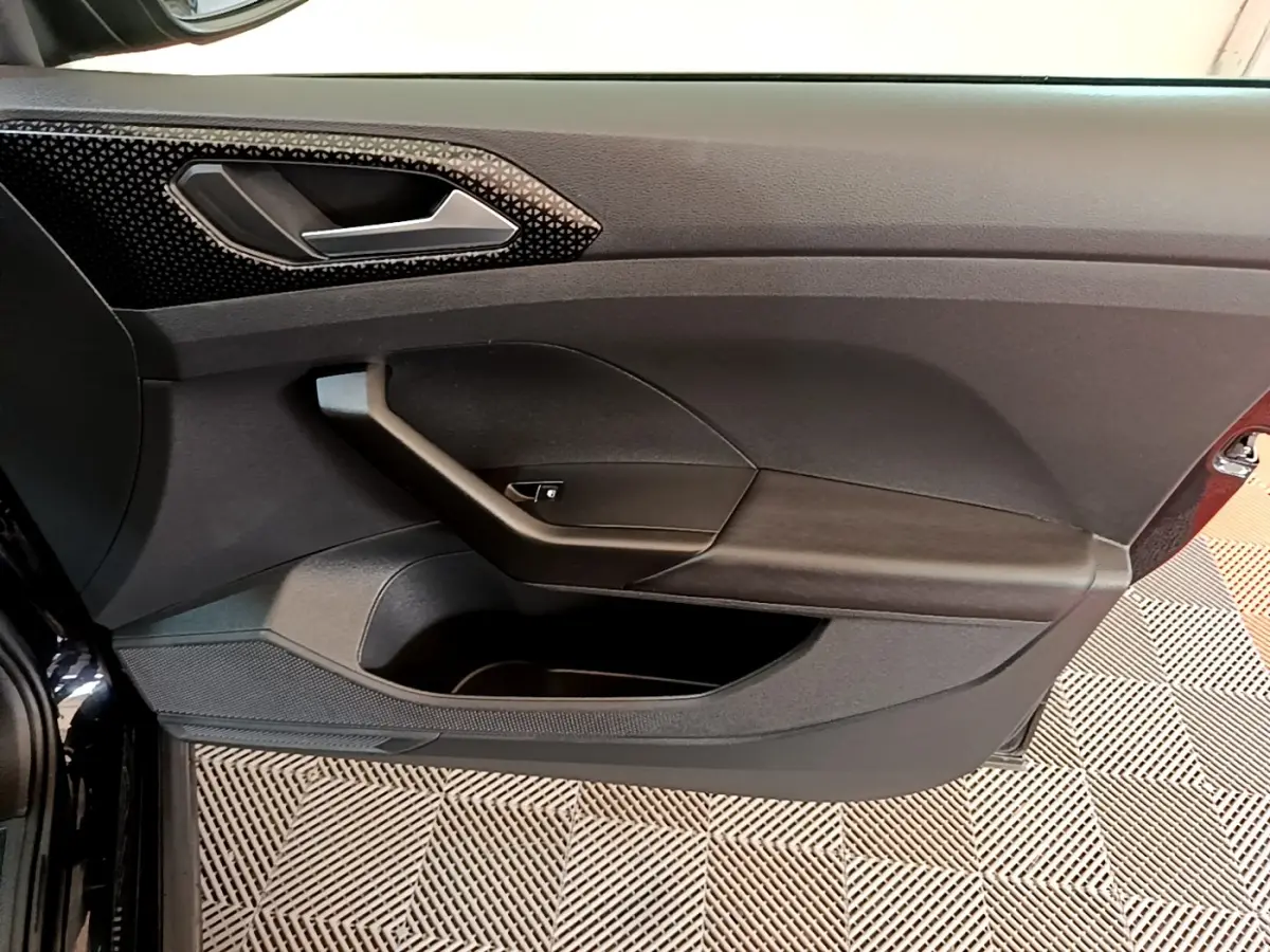 Vue rapprochée de la porte intérieure côté conducteur du Volkswagen T-Cross noir, avec poignée et rangement intégré.