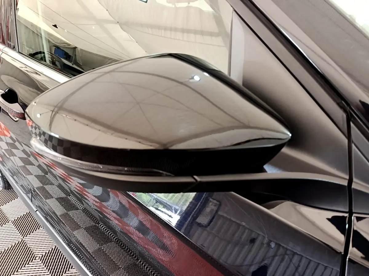 Gros plan sur le rétroviseur droit noir brillant du Volkswagen T-Cross 2022 avec reflet de l'environnement intérieur.
