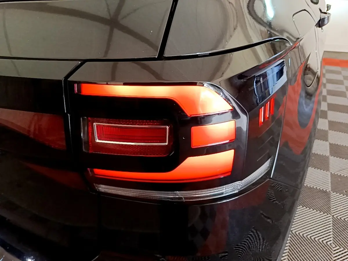 Gros plan sur le feu arrière droit rouge allumé d’un Volkswagen T-Cross noir, avec reflet sur la carrosserie brillante.
