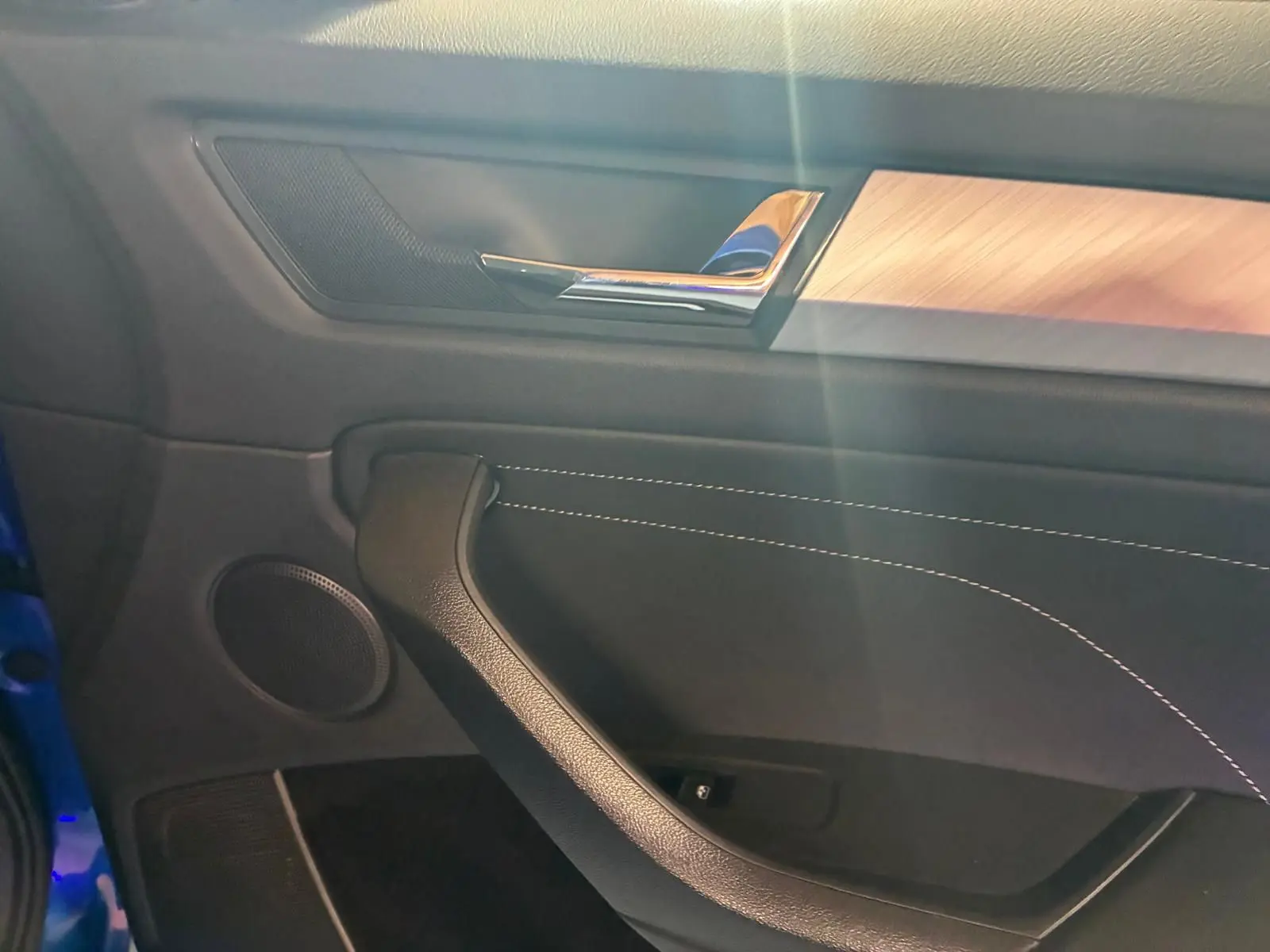 Détail de la porte côté gauche du Skoda Kodiaq 2023 bleu, avec garniture noire, surpiqûres blanches et insert bois clair.