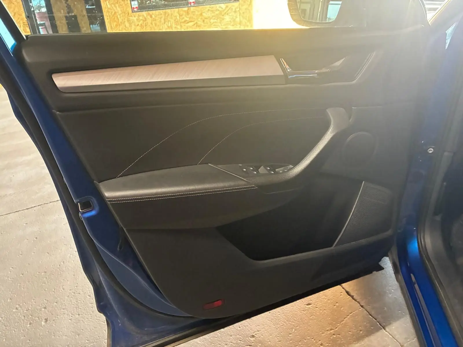 Vue intérieure de la porte avant gauche d’un Skoda Kodiaq bleu 2023, avec garniture noire et insert bois clair.