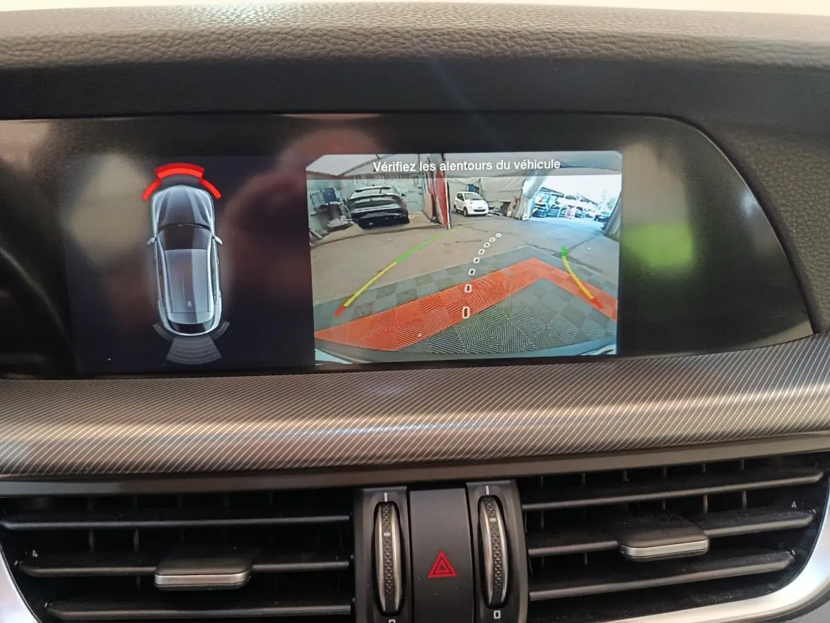 Écran central de l'Alfa Romeo Stelvio gris foncé montrant la caméra de recul avec aide au stationnement arrière.
