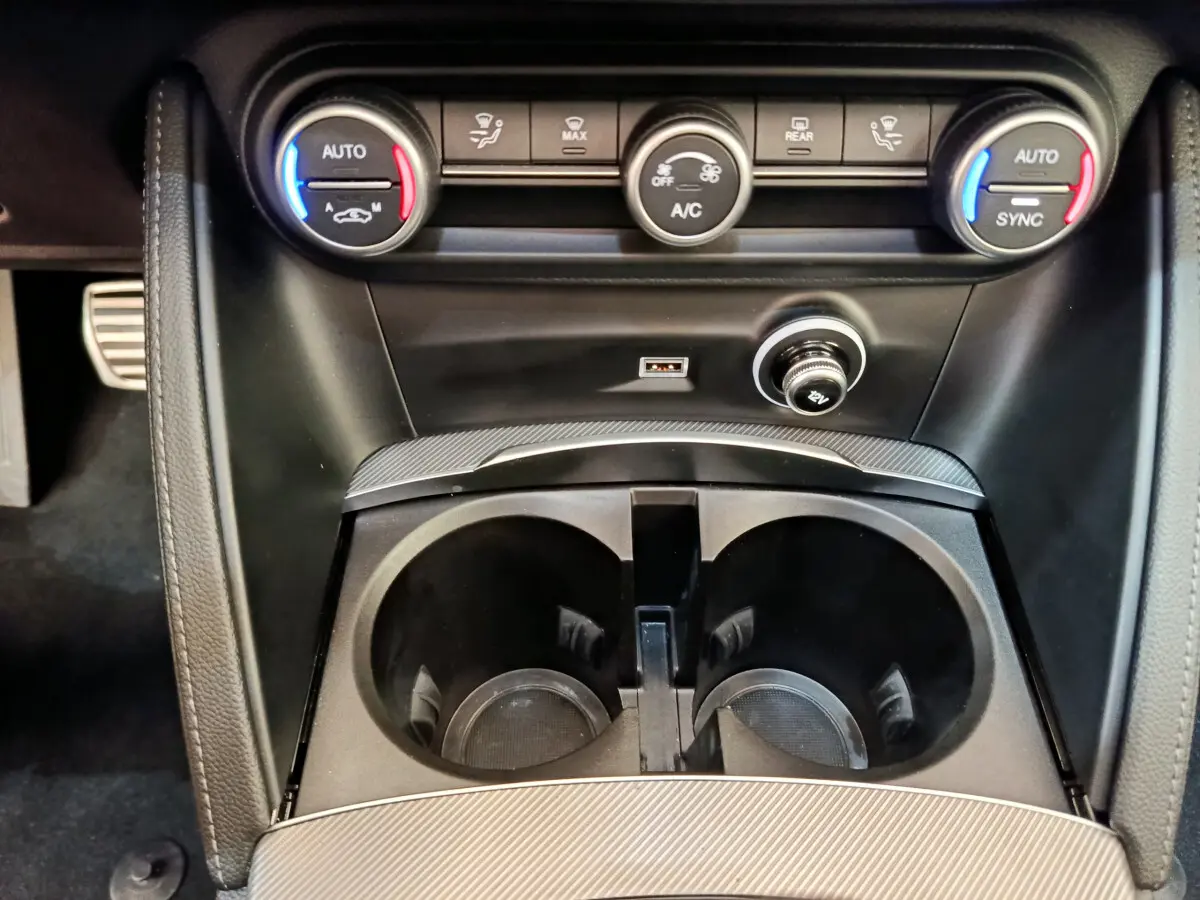 Gros plan sur la console centrale noire avec commandes climatisation bi-zone et prises USB du Alfa Romeo Stelvio Sprint 2024.